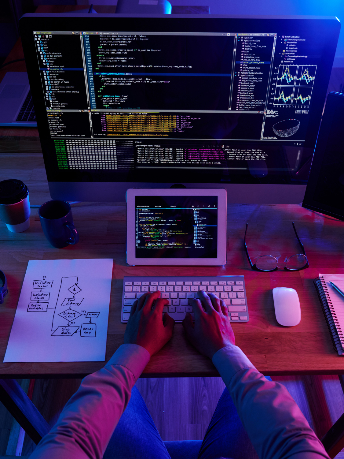 A developer working at a desk with code on screen and a hand-drawn process flow beside the keyboard.